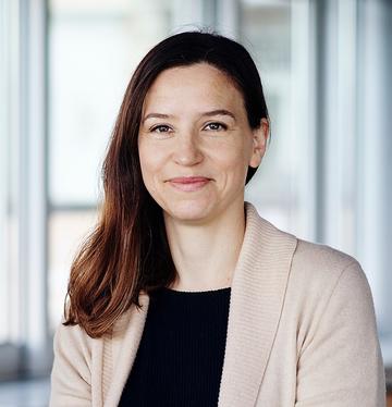 Rachael garret A white woman with long dark hair smiles at the camera. She wears a cream cardigan over a black shirt.