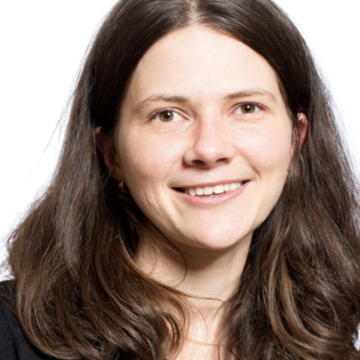 A white woman with long brown hair and brown eyes smiles at the camera.