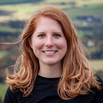 Lindsay jaacks A red-haired white woman stands smiling in the photo, with a view of a valley behind her