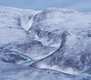 Blue meltwater cuts a jagged path through an icy landscape