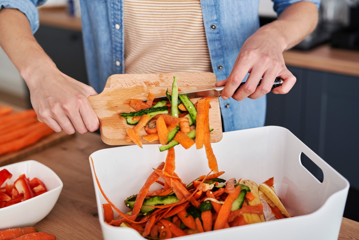 A woman scraps vegetable peelings from a board into a container